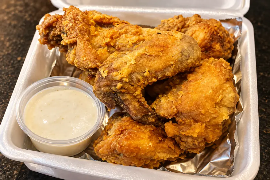 Buttered Chicken pieces in a takeout box with a cup of dipping sauce